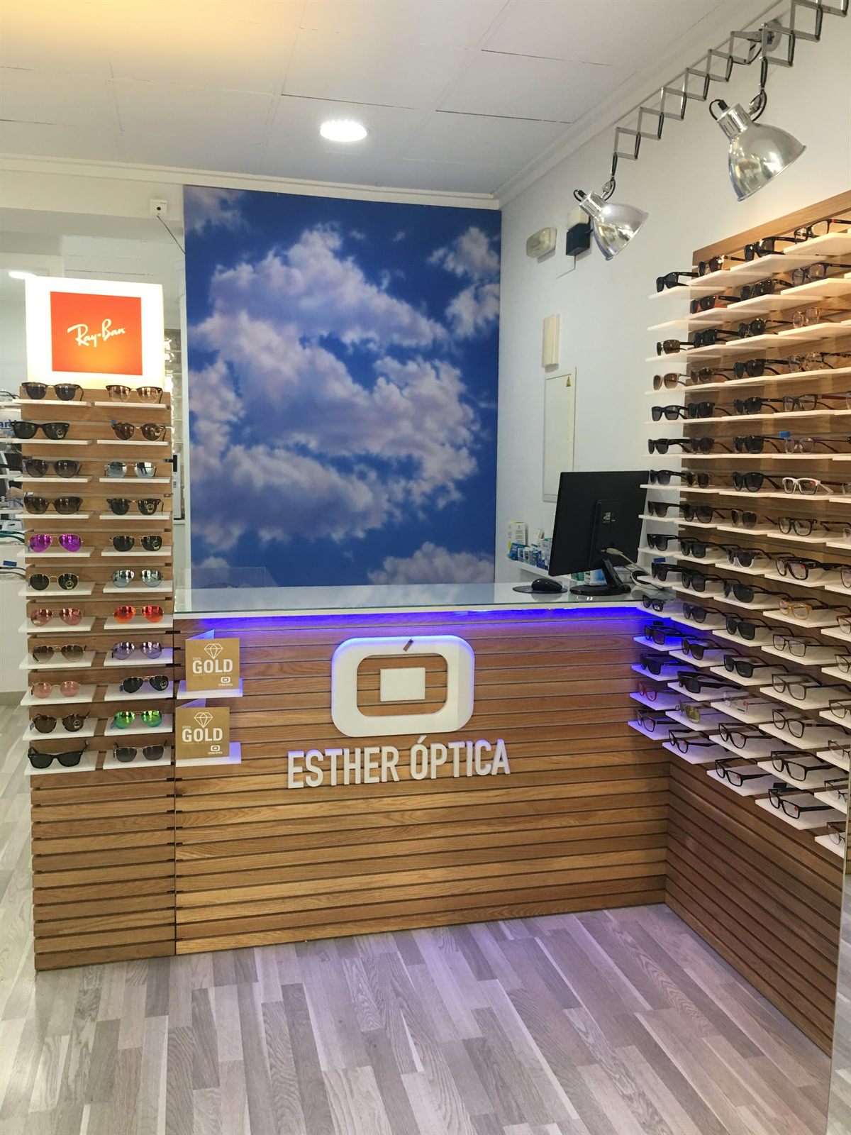 Mostrador de Esther Óptica con el logotipo corpóreo y el mural de nubes al fondo