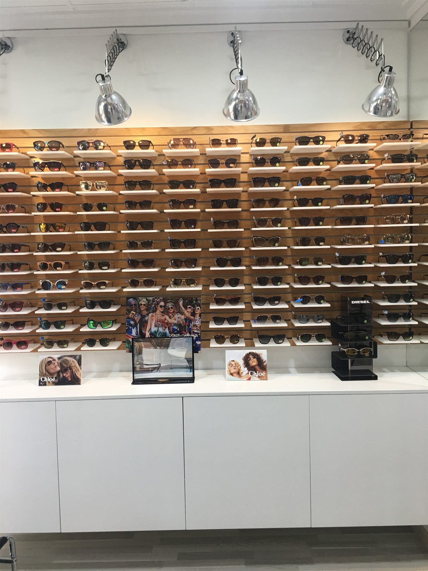 Pared de gafas de sol expuestas sobre estantes de madera en Esther Óptica