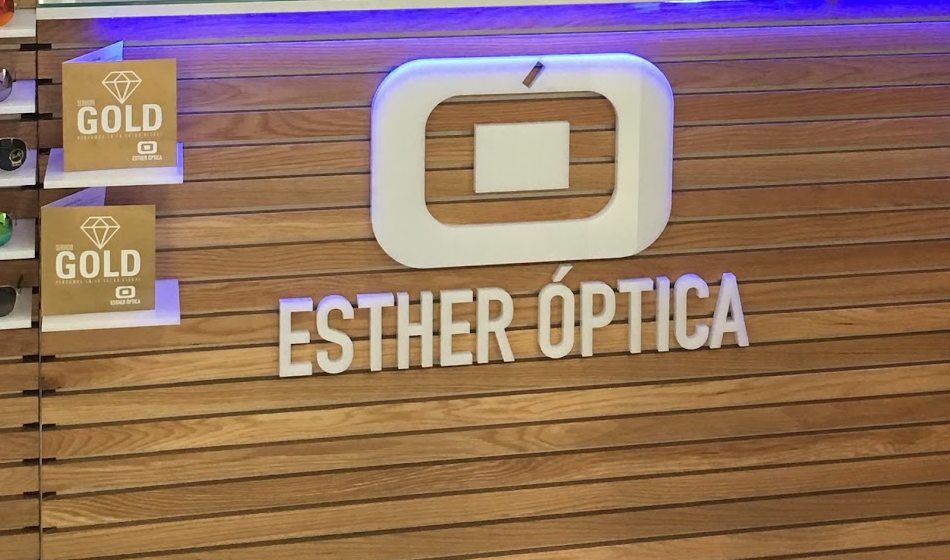 Letras corpóreas y logotipo de Esther Óptica sobre la pared de madera del mostrador